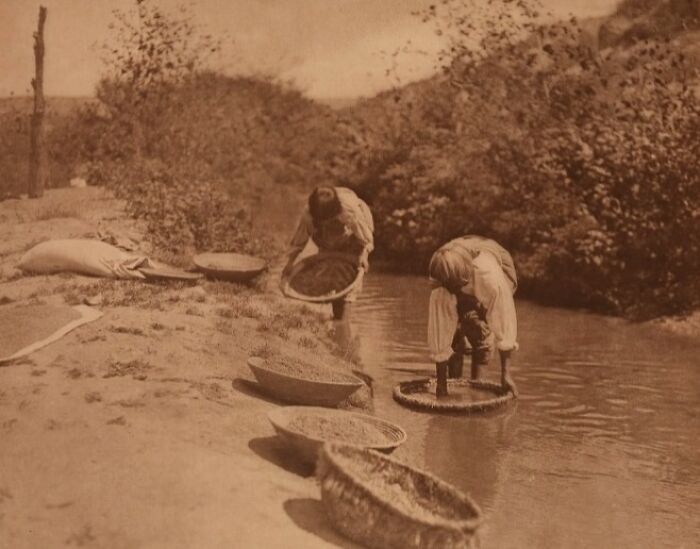 Two Native Americans washing baskets in a river, an Edward S. Curtis photo preserving Native American history.