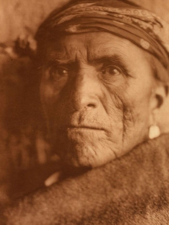 Close-up sepia portrait of a Native American elder wearing a patterned headband, from Edward S. Curtis photos preserving history.