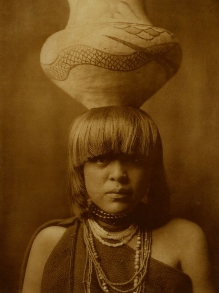 Native American woman with traditional hairstyle and pottery on head in a powerful Edward S Curtis photo preserving history.