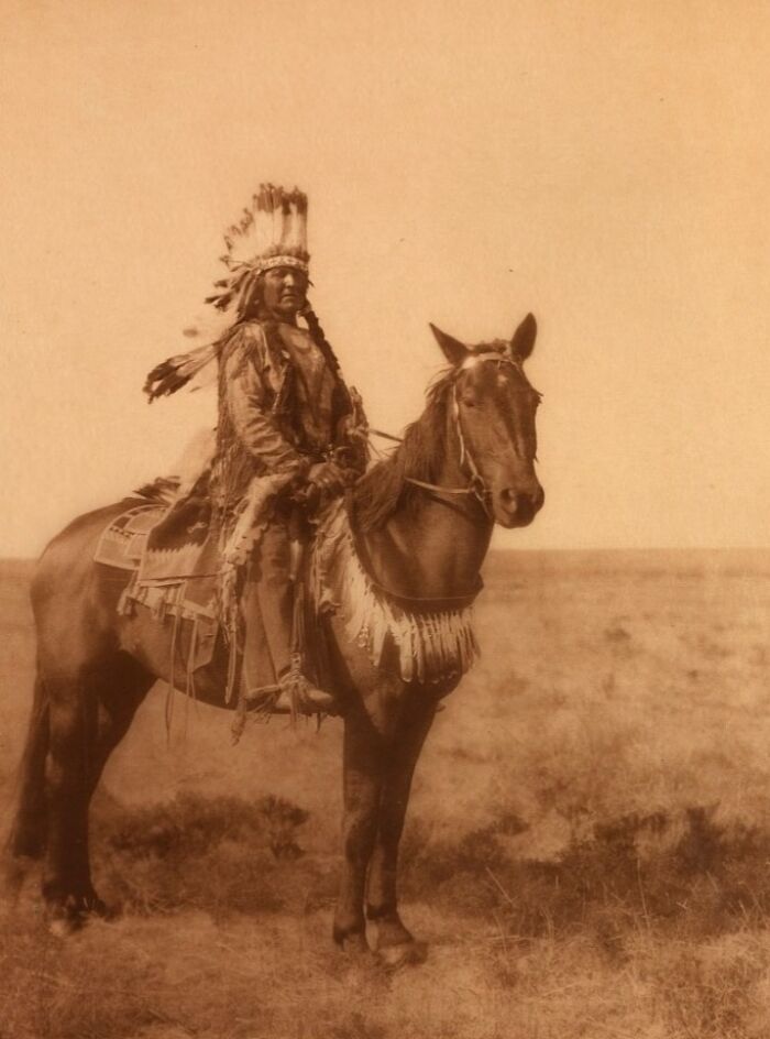Native American man in traditional attire on horseback in a sepia-toned Edward S. Curtis photo preserving history.