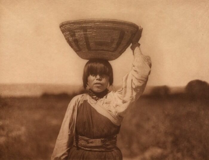 Native American woman carrying woven basket on head, captured in a powerful Edward S. Curtis photo preserving history.
