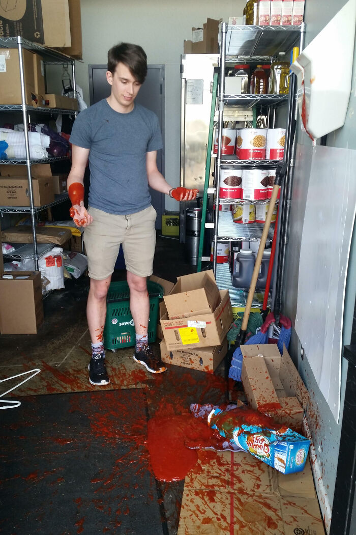 Young man in storage room covered in spilled tomato sauce, illustrating an epic work fail in a messy workplace environment.