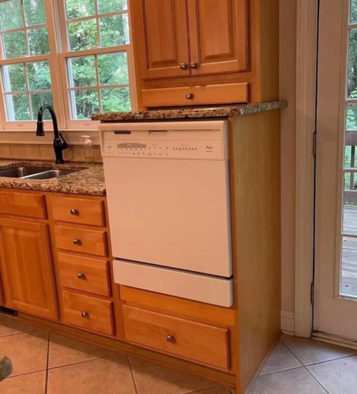 Kitchen dishwasher placed awkwardly inside wooden cabinets showing a failed creative home design attempt.