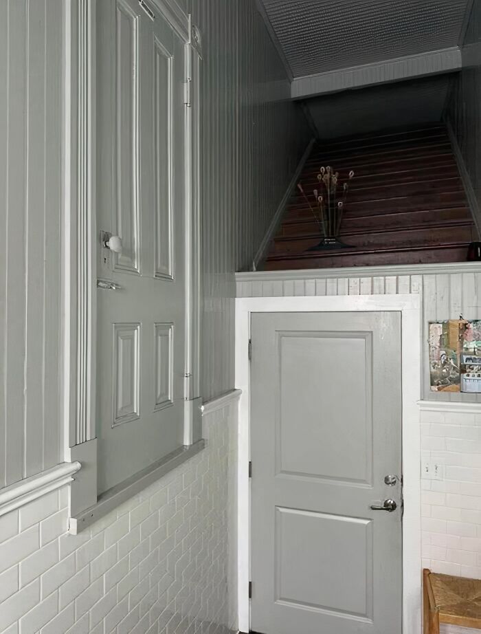 Small gray door under wooden stairs with an unreachable door above, showing a failed creative home design attempt.