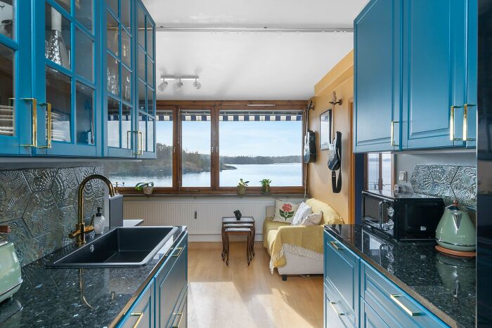 Bright living space revamp featuring blue kitchen cabinets, modern black countertops, and a cozy seating area with lake view.