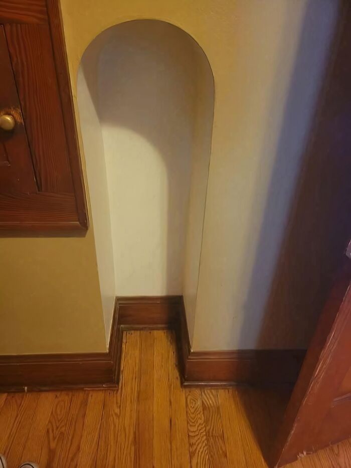 Niche home design with a small, unexplained recessed archway and mismatched wooden baseboard trim on hardwood floor.