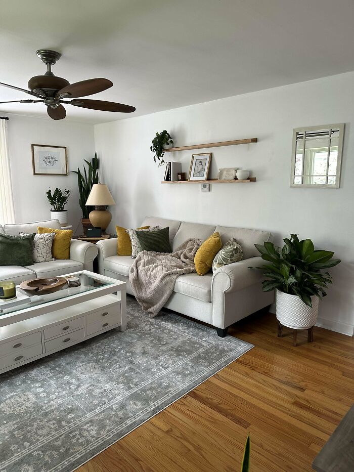 Cozy living space revamped with neutral sofas, green and yellow pillows, plants, and minimalist wall shelves in a bright room.