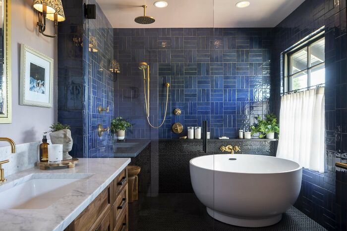 Modern bathroom living space revamp featuring blue tiles, gold fixtures, a round bathtub, and natural light from a large window.