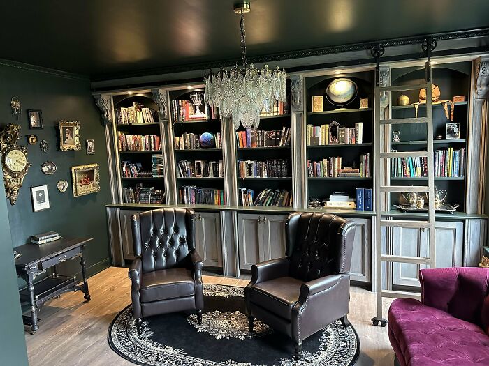 Cozy living space revamped with dark wood bookshelves, leather armchairs, chandelier, and elegant vintage decor.