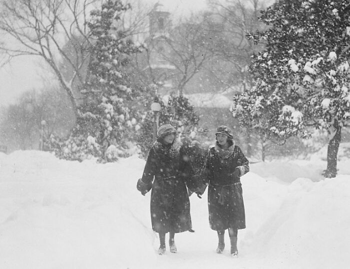 Two women dressed in 1920s attire walking through heavy snow in Washington, D.C., vintage US winter scene.