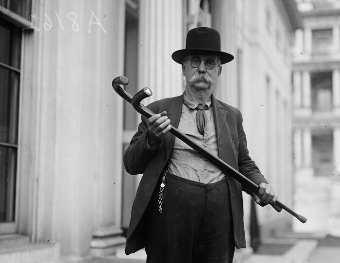 Vintage photo of a man with a mustache and hat holding walking sticks in historical Washington, D.C. from the 1920s.