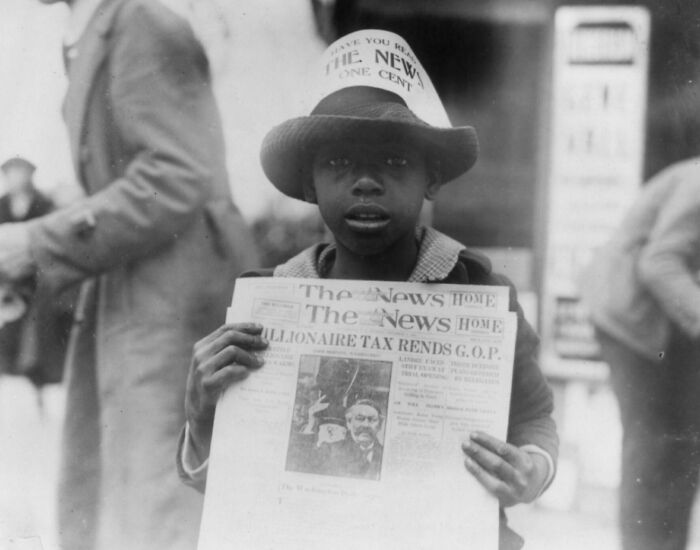 Vintage photo of a boy selling newspapers on a street in Washington, D.C., capturing 1920s US historical life.