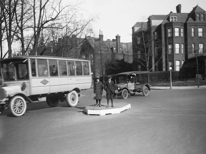 Two children standing on a traffic island with vintage cars in a 1920s Washington, D.C. street scene.