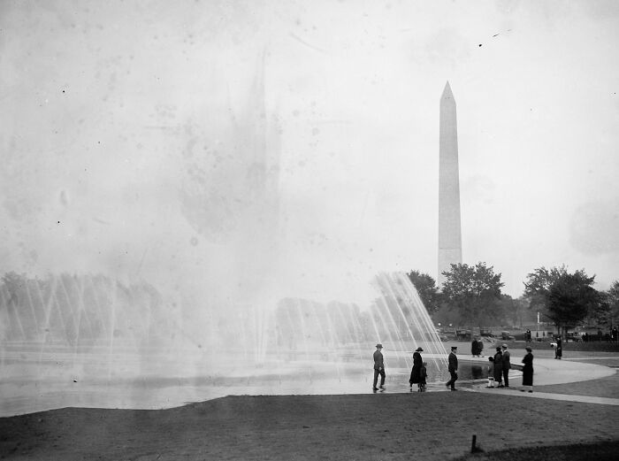 Vintage black and white photo of Washington D.C. fountain with people and Washington Monument in the background, 1920s.