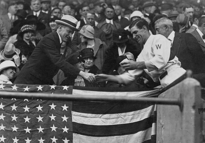 Vintage black and white photo showing a crowd and a man shaking hands at a 1920s Washington, D.C. event.