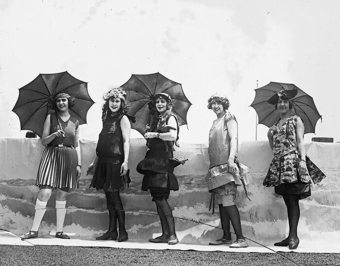 Five women in 1920s dresses holding umbrellas, posing outdoors in a vintage Washington D.C. photo.