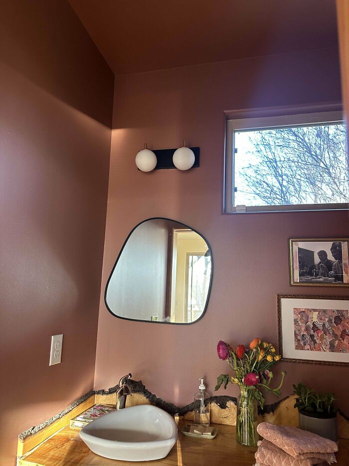 Modern living space revamp with unique mirror, stylish sink, warm lighting, and floral decor in a cozy bathroom corner.