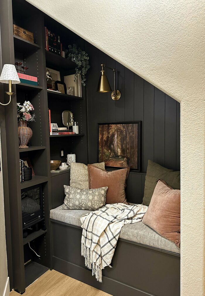 Cozy living space revamp with built-in dark wood shelves, cushioned bench, throw blanket, decorative pillows, and warm lighting.