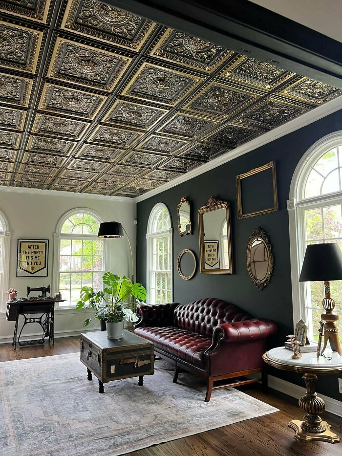 Living space revamped with a vintage leather sofa, ornate ceiling tiles, antique mirrors, and cozy natural lighting.