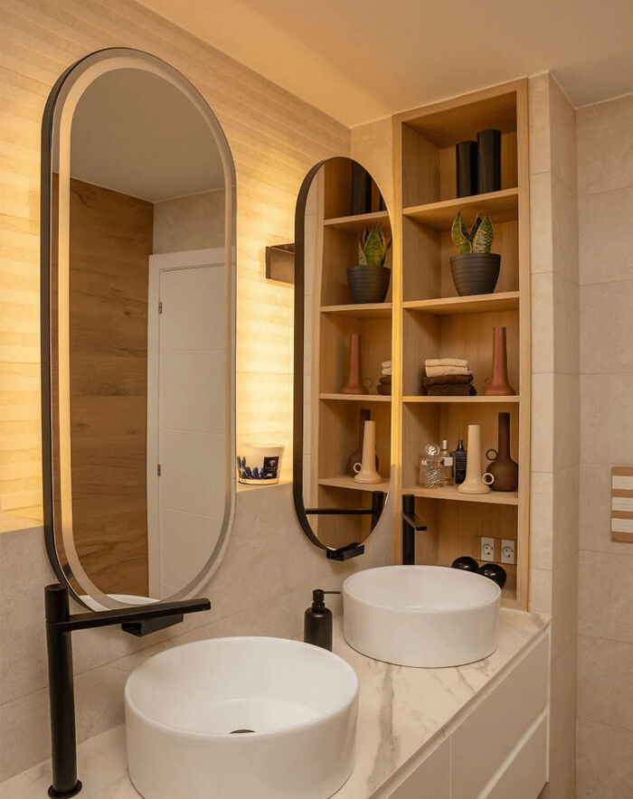 Modern bathroom revamp with dual oval mirrors, vessel sinks, and wooden shelves showcasing decor and plants.