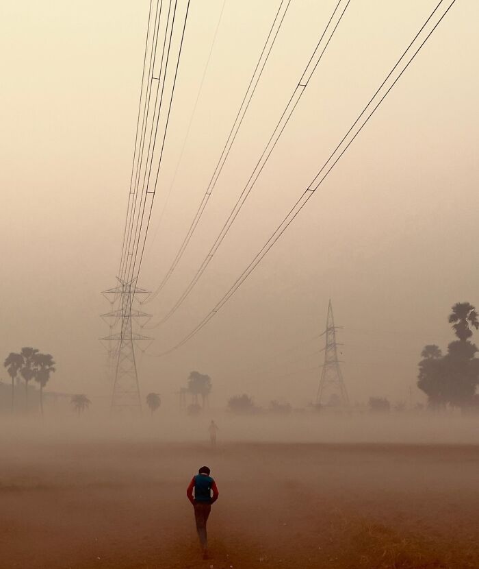 Man walking through foggy field under power lines at sunrise, capturing the essence of explore Asia photography.