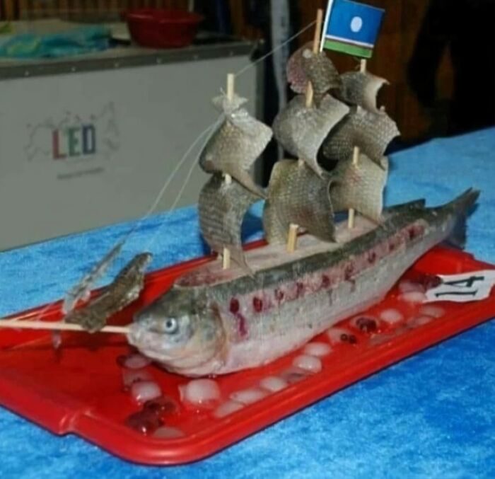 Fish crafted into a cursed food ship with scales as sails on a red tray with ice, showing unusual food art presentation.