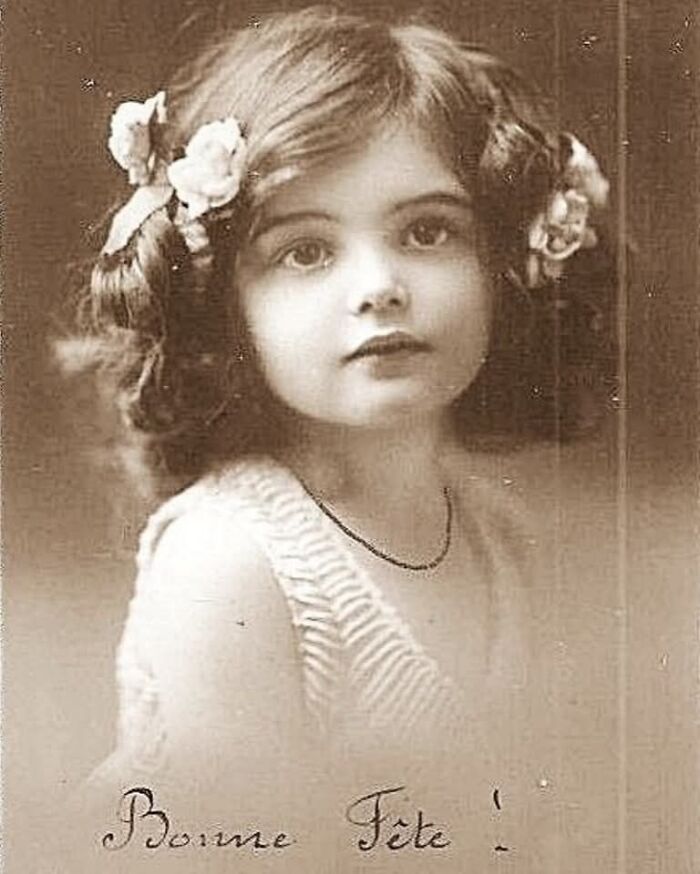 Sepia-toned fascinating historical photo of a young girl with curly hair and flowers, capturing past innocence and charm.