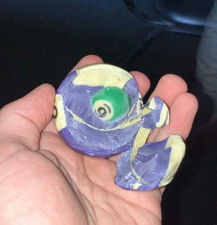 Hand holding a mildly interesting broken purple and yellow spiral object with a green eye-like center.