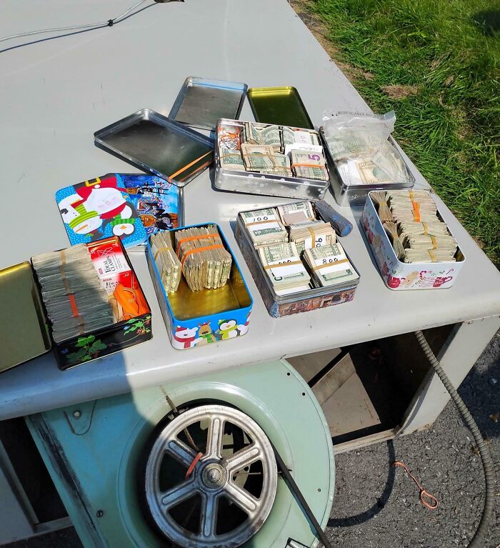 Multiple tins filled with bundles of cash, showcasing a mildly interesting collection of money on a table outdoors.