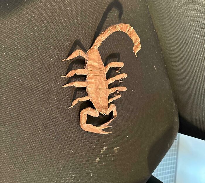 Intricately folded origami scorpion resting on a dark fabric surface, showcasing mild interesting craftsmanship and detail.