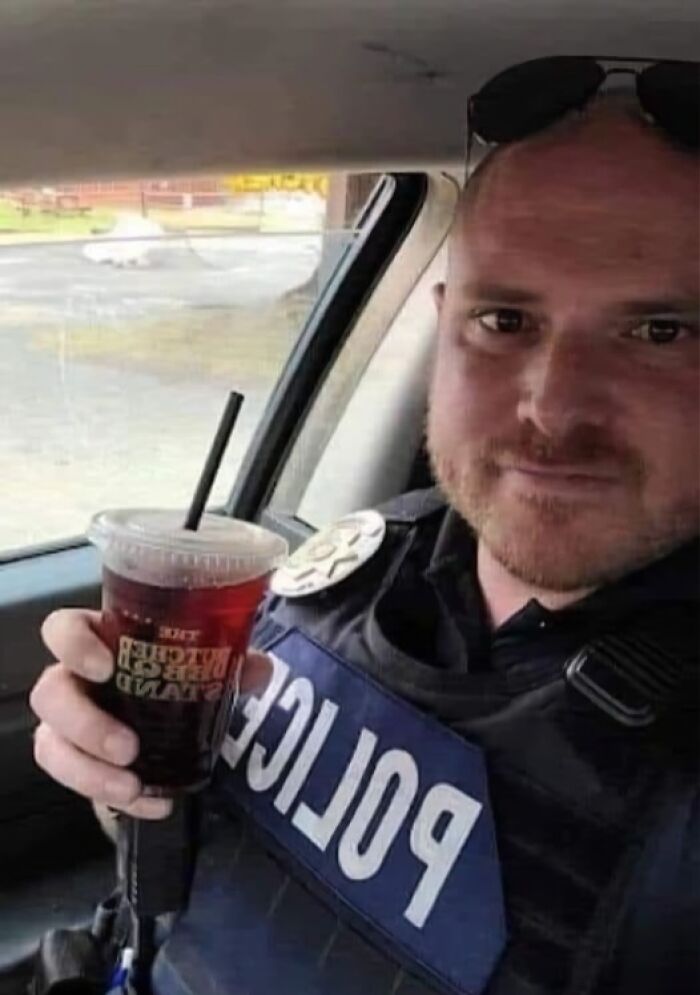 Police officer in uniform sitting in a car holding a drink, showcasing a wholesome moment in the wonderful world.
