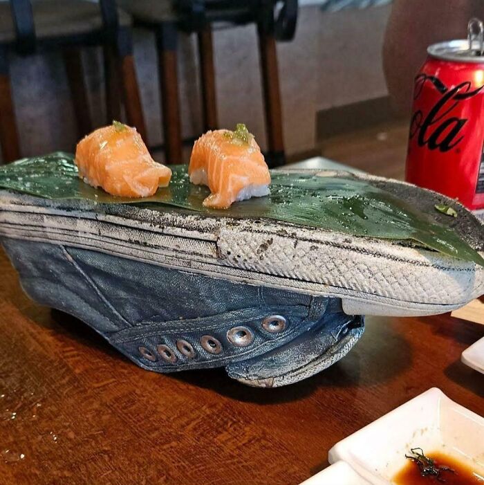 Two pieces of sushi served on a green leaf placed on an old worn sneaker as an unholy meal presentation.
