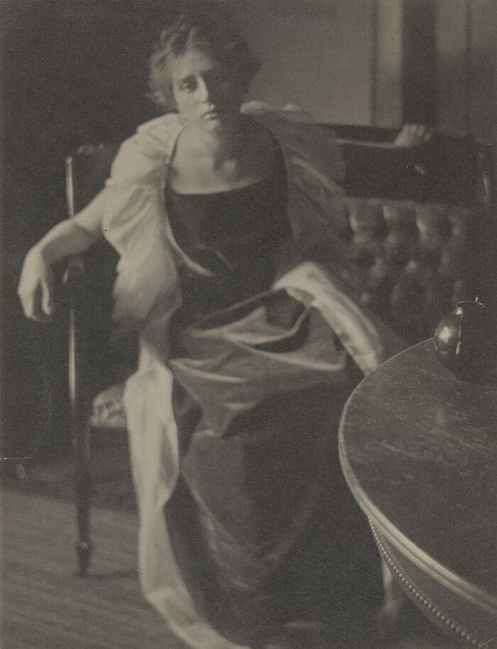 Vintage black and white photo of a woman from the 1900s sitting on a chair, showcasing the beauty of women era style.