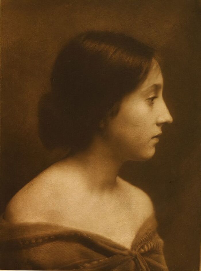 Sepia-toned old photo of a woman from the 1900s showing classic beauty in profile with her hair styled back.