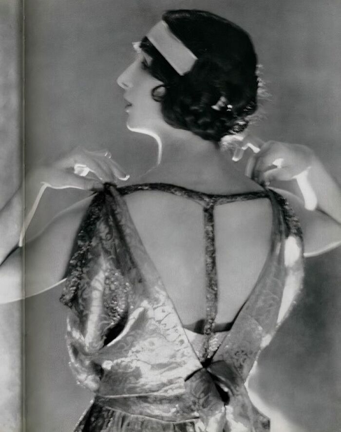 Black and white portrait of a woman from the 1900s adjusting her vintage dress, highlighting the beauty of women from that era.