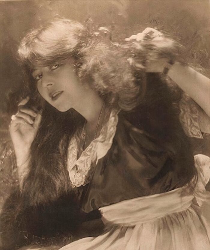 Sepia-toned old photo of a woman from the 1900s with long hair and vintage clothing showcasing timeless beauty.