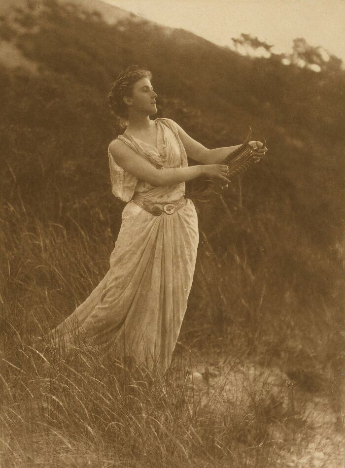 Sepia-toned vintage photo of a woman in a flowing dress playing a harp outdoors, showcasing beauty of women 1900s.