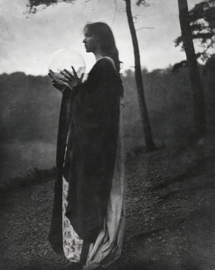 Black and white vintage photo of a woman from the 1900s holding a glowing orb in a dark outdoor setting.