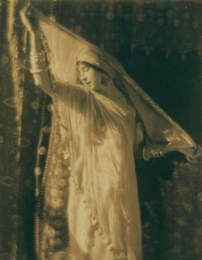 Vintage photo of a woman from the 1900s gracefully posing with a flowing veil, showcasing beauty and elegance.