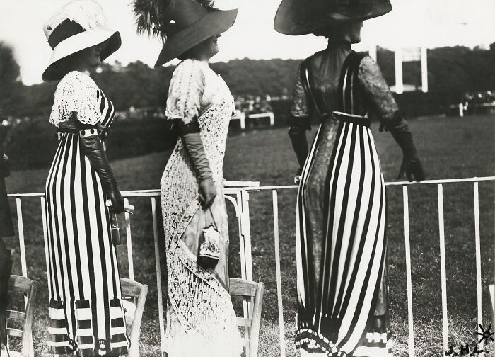 Three women in 1900s striped and lace dresses with large hats showing the beauty of women from the early 1900s.
