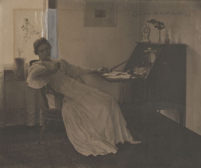 Vintage photo of a woman in a flowing dress seated by a desk, capturing the beauty of women from the 1900s.