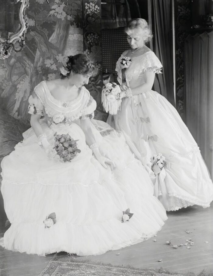 Two women in elegant 1900s dresses holding bouquets, showcasing the beauty of women from the early 20th century.