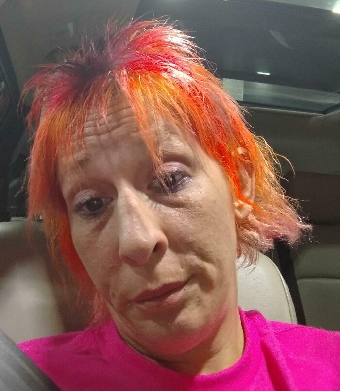 Person with bright orange and pink hair in a car after a salon visit, capturing a glow-up and breakdown moment.