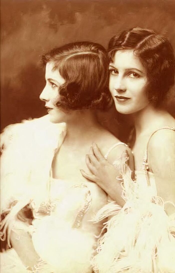 Two elegant women from the 1900s with vintage hairstyles and feathered attire showcasing beauty and style.