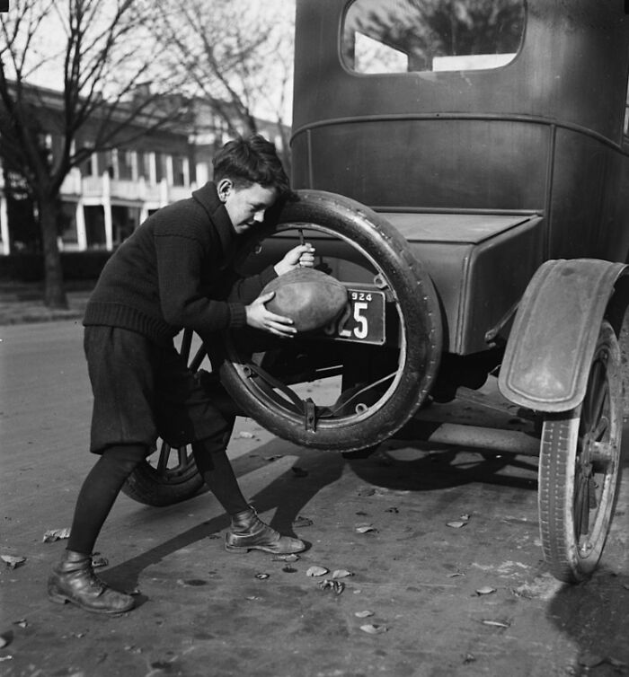 Boy in vintage clothing changes car tire in Washington DC street in historical black and white photo from 1920s era.