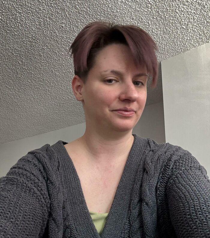 Person with short hair and a gray knitted sweater taking a selfie, illustrating salon glow-up and breakdown experiences.