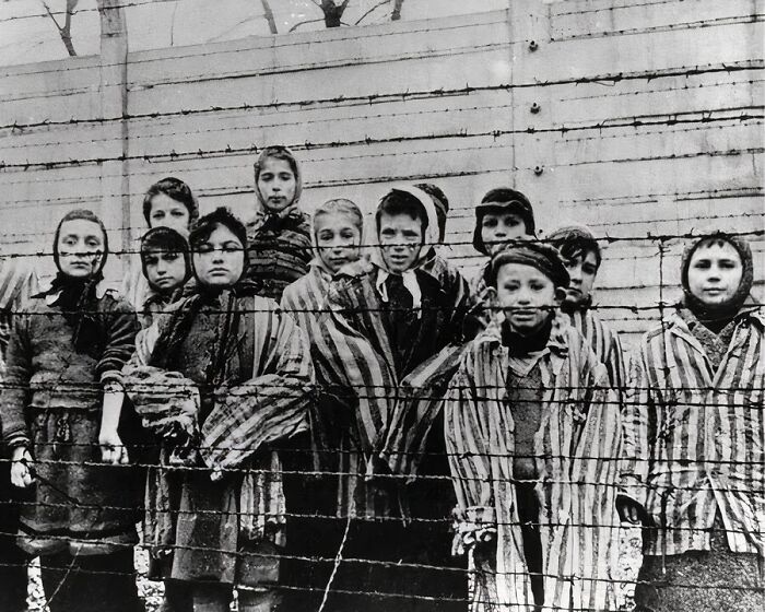 Group of children behind barbed wire wearing striped clothing in a unique old photo capturing a historical moment.