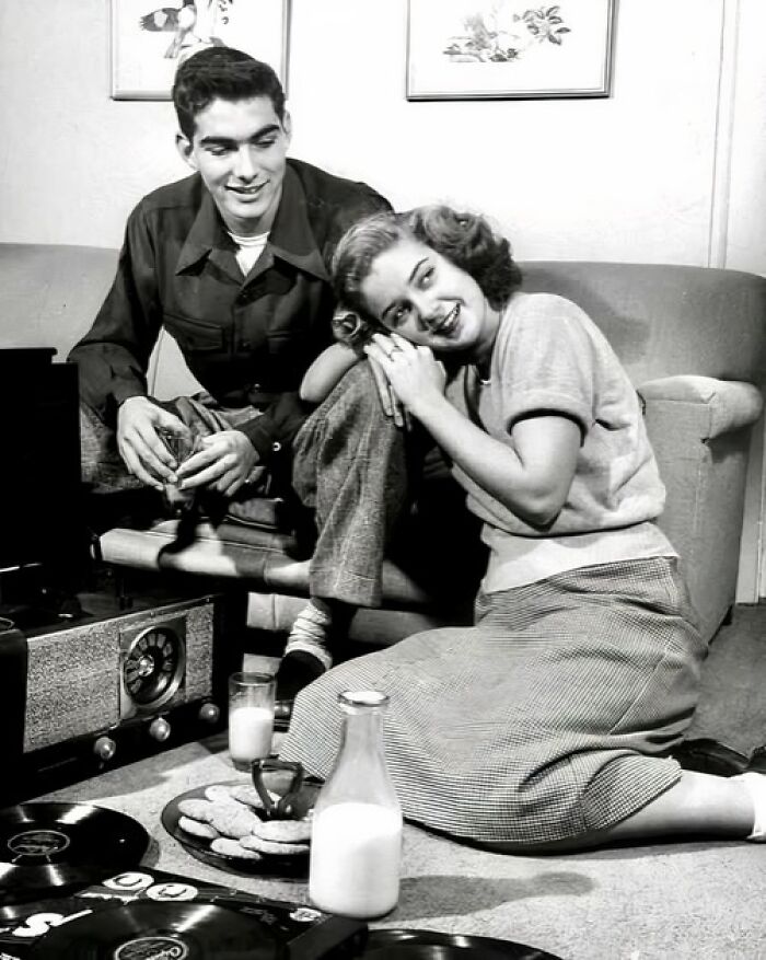 Young couple enjoying music and snacks in a vintage living room, a unique old photo capturing a candid moment.