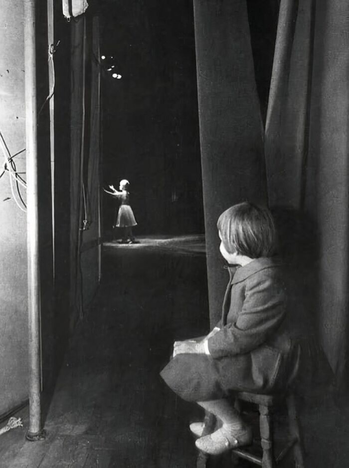 Young girl backstage watching a ballet performance in a unique old photo capturing a rare moment behind the scenes.