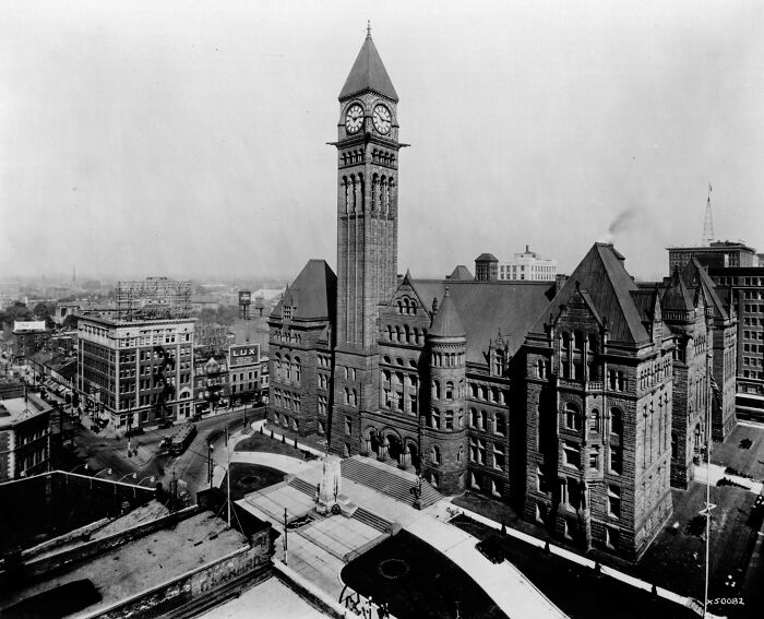 Historic photograph showing a cityscape with a prominent clock tower and surrounding buildings from 100 years ago.